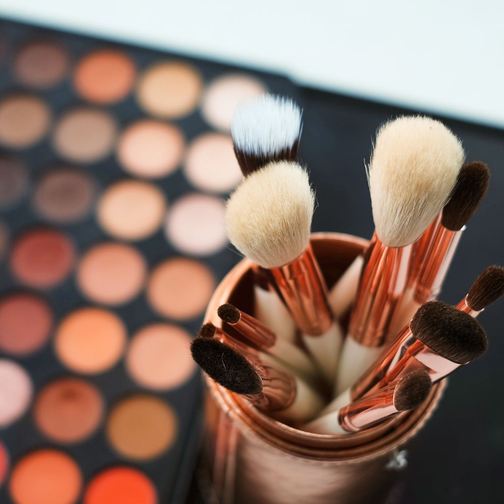 Makeup brushes in a holder with a blurred makeup palette in the background