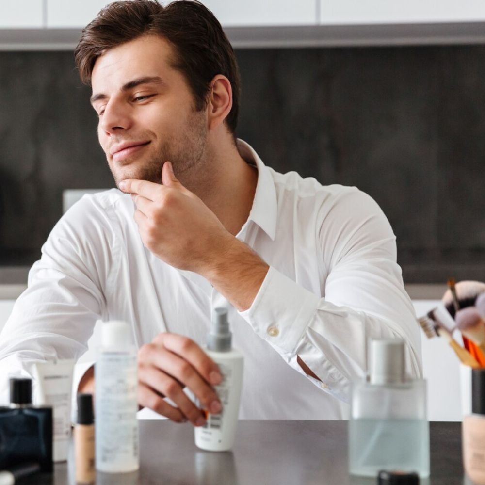 Man in a kitchen examining skincare products on a counter