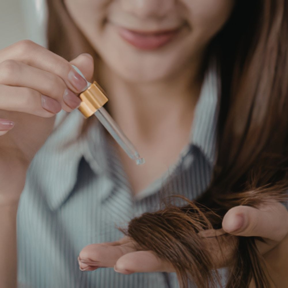 Person applying a dropper of oil to their hair